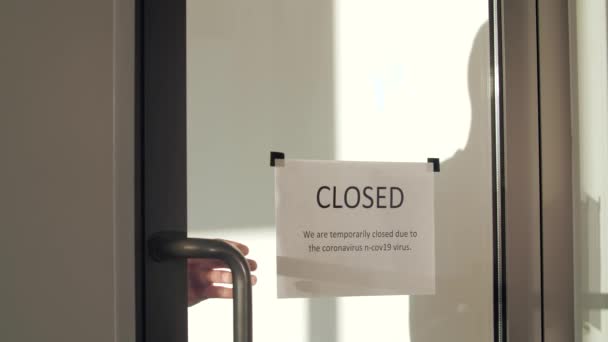 Een knappe gemaskerde man loopt naar de glazen deur en rukt het gesloten bord eraf. Heropening voor bedrijven past zich aan nieuw normaal aan in de nieuwe Coronavirus COVID-19 pandemie. - Video