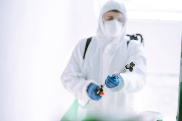Man wearing protective suit disinfecting the entrance of a residential building with spray chemicals to preventing the spread of coronavirus, pandemic in quarantine city. Covid -19. Cleaning concept. - 写真・画像