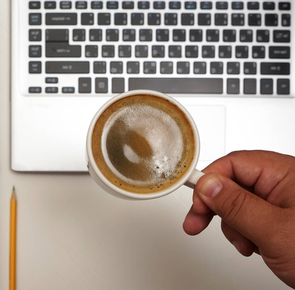 Top view of male hand with  coffee cup above laptop. empty brown notebook with yellow pencil.  - Φωτογραφία, εικόνα