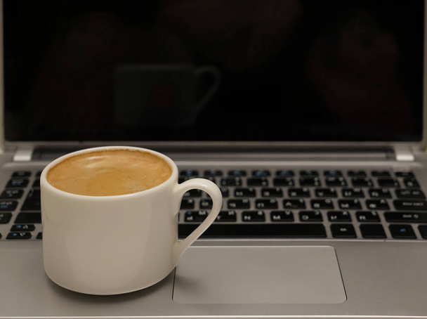 White Cup of coffee with pattern on the foam. Hot freshly brewed coffee in a white mug on gray laptop. empty black screen.  - Foto, Imagem