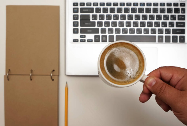  Top view of male hand with  coffee cup above laptop. empty brown notebook with yellow pencil.  - Fotografie, Obrázek