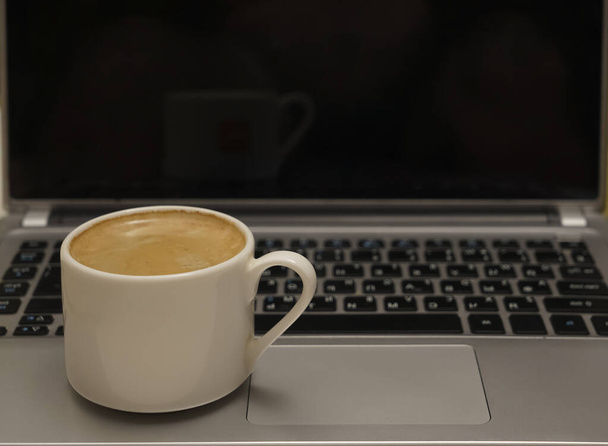White Cup of coffee with pattern on the foam. Hot freshly brewed coffee in a white mug on gray laptop. empty black screen.  - Foto, Imagem