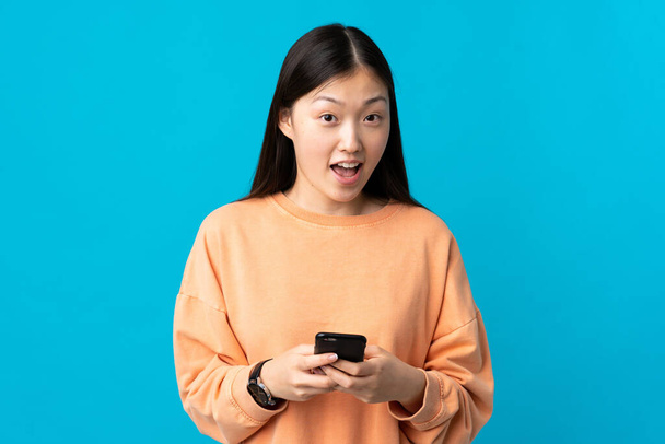 Young Chinese girl over isolated blue background surprised and sending a message - Φωτογραφία, εικόνα