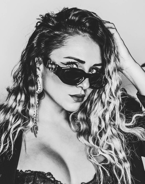 Retrato en blanco y negro de un modelo alternativo con cabello rubio rizado usando gafas de sol - Foto, Imagen