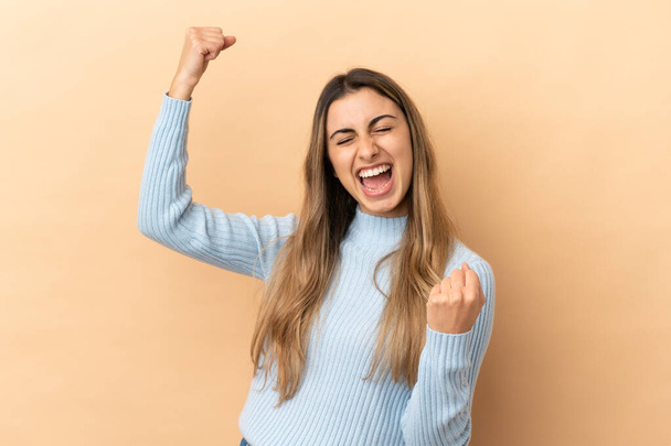 Young caucasian woman isolated on beige background celebrating a victory - Photo, Image