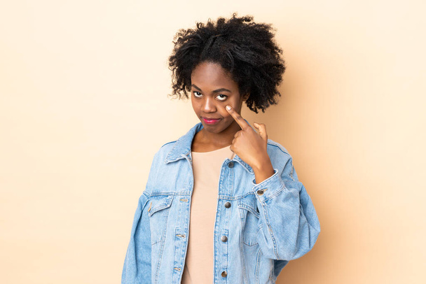 Νεαρή Αφρο-Αμερικανίδα απομονωμένη σε μπεζ φόντο που δείχνει κάτι - Φωτογραφία, εικόνα