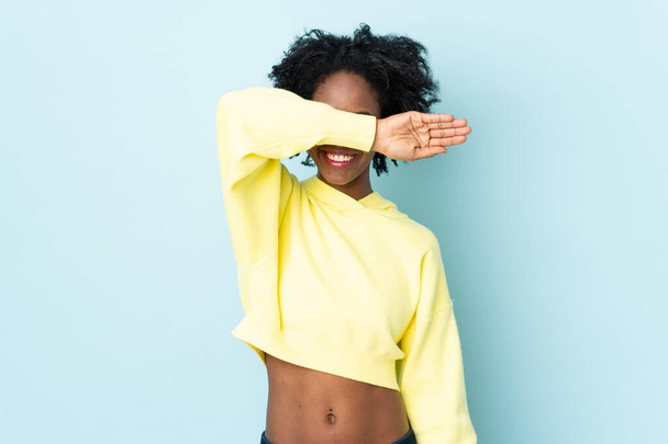 Νεαρή Αφρο-Αμερικανίδα απομονωμένη σε μπλε φόντο που καλύπτει τα μάτια με τα χέρια - Φωτογραφία, εικόνα