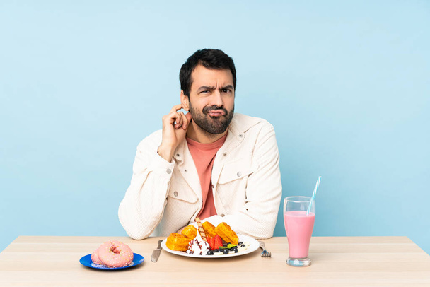 Man aan tafel met ontbijt wafels en een milkshake met twijfels - Foto, afbeelding