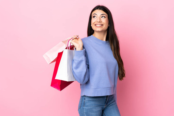 Young brunette girl over isolated pink background holding shopping bags and smiling - Photo, Image
