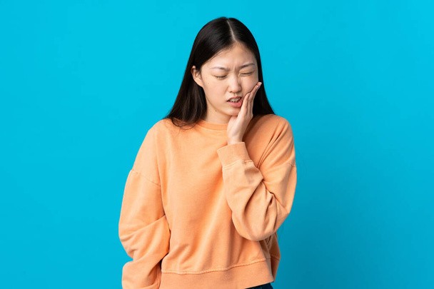 Fiatal kínai lány izolált kék háttér fogfájás - Fotó, kép
