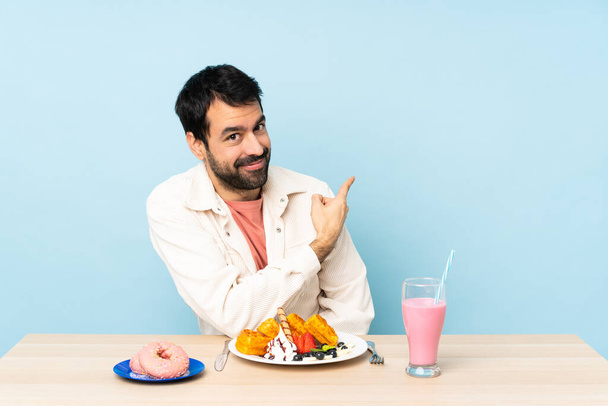 Человек за столом, завтракающий вафлями и молочный коктейль, указывающий назад - Фото, изображение