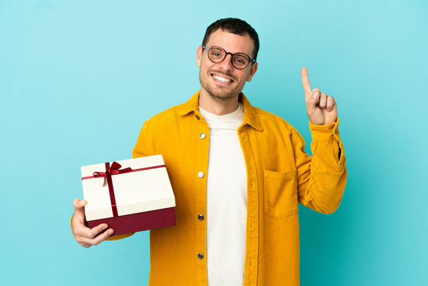 Brazilian man holding a gift over isolated blue background pointing up a great idea - Fotó, kép