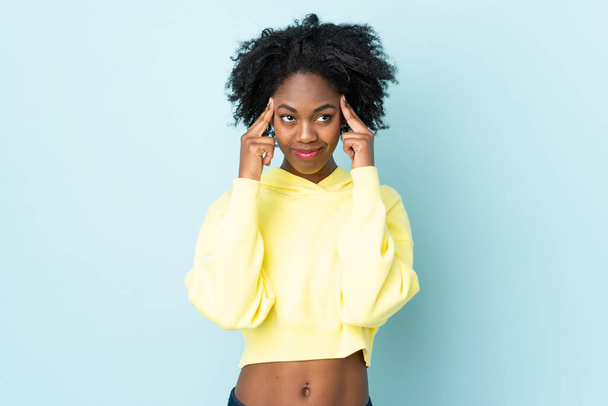 Nuori afroamerikkalainen nainen eristetty sinisellä taustalla, jolla on epäilyksiä ja ajattelua - Valokuva, kuva