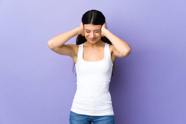 jonge brunette vrouw over geïsoleerde paarse achtergrond gefrustreerd en het bedekken van oren - Foto, afbeelding