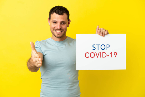 Brazilian man over isolated purple background holding a placard with text Stop Covid 19 making a deal - Foto, Bild
