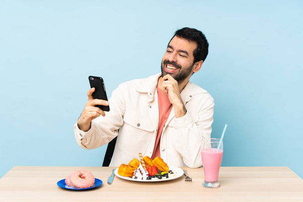 Mies pöydässä syömässä vohveleita ja pirtelö tekemässä selfietä. - Valokuva, kuva