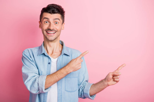 Photo of amazed handsome young brunette man point index finger empty space wear blue shirt isolated on pastel pink color background - Foto, Imagem