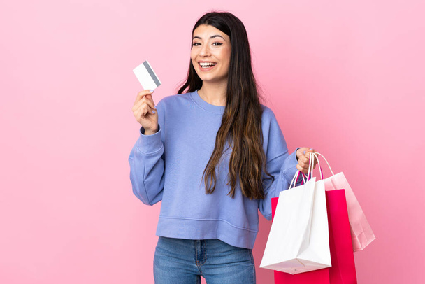 Joven morena sobre fondo rosa aislado sosteniendo bolsas de compras y una tarjeta de crédito - Foto, imagen