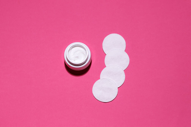 crema cosmética y discos de algodón sobre un fondo de estudio rosa - Foto, Imagen
