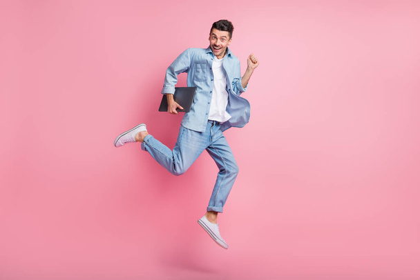 Full size photo of excited happy man hold laptop jump air run sale wear jeans isolated on pink color background - Photo, Image