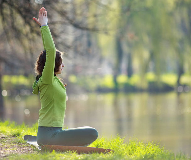 Young woman meditates, practices yoga, on the river bank against the background of beautiful nature - Foto, Imagen