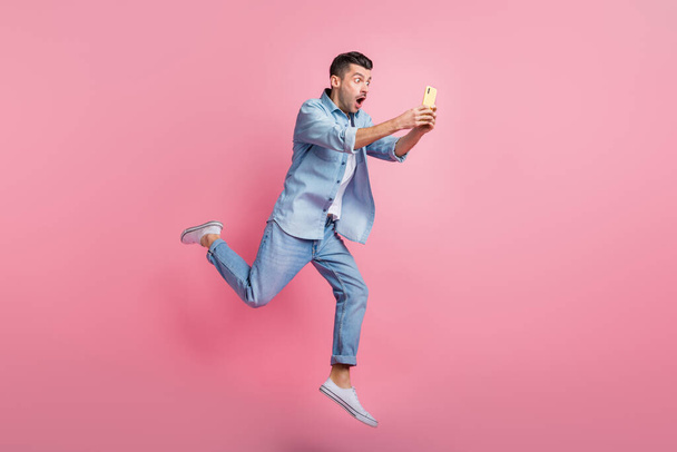 Full body photo of brunette man hold phone amazed news run jump wear casual outfit isolated on pink color background - Photo, Image