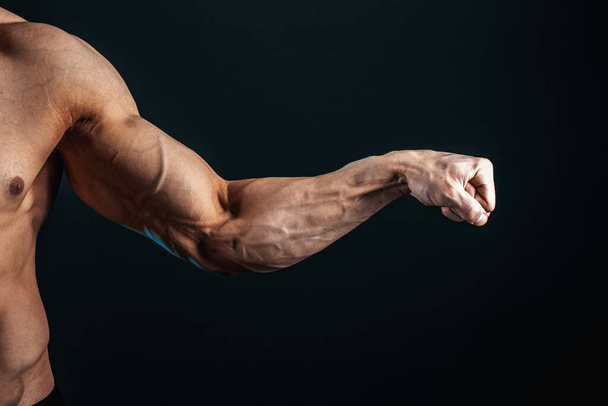 tense arm clenched into fist, veins, bodybuilder muscles on a dark background, isolate - Photo, image