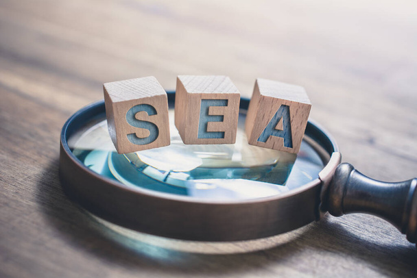 Lupa vintage com blocos de mar em uma mesa de madeira antiga - Search Engine Advertising Concept - Foto, Imagem