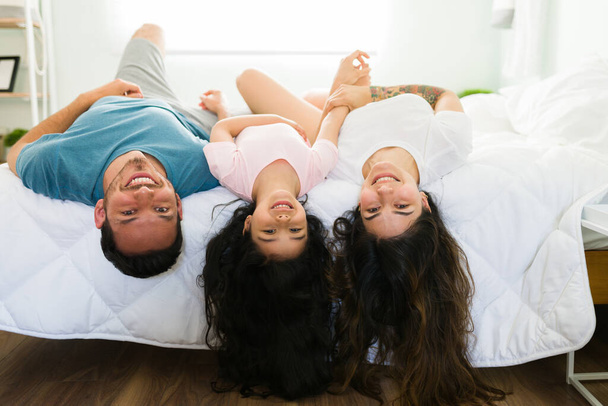 Retrato de una hermosa familia hispana en pijama acostada boca abajo en la cama mientras sonríe y hace contacto visual  - Foto, imagen