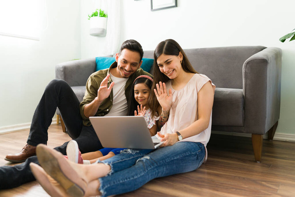 Glückliche Eltern und Tochter winken und grüßen ihre Familie und Großeltern bei einem Online-Videoanruf zu Hause - Foto, Bild