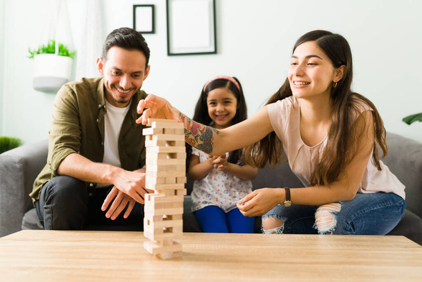 Zabawa szczęśliwa rodzina gra planszowa z drewnianymi blokami wieży. Dziewczynka bawi się z rodzicami w salonie - Zdjęcie, obraz