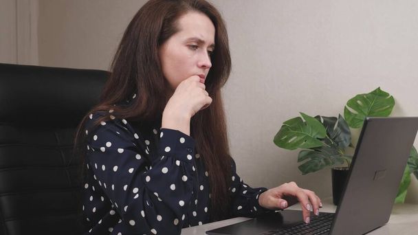 Een vermoeide volwassen vrouw werkt als freelancer op afstand in haar kantoor, een zakenvrouw doet een online project op een computer in een applicatie, communicatie via sociale netwerken, een onafhankelijke gratis - Foto, afbeelding