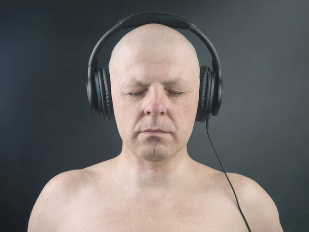 muž se zavřenýma očima poslouchá hudbu se sluchátky na tmavém pozadí - Fotografie, Obrázek