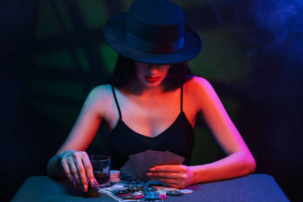 gioco d'azzardo ragazza in un cappello e vestito gioca a poker a un tavolo con carte, patatine fritte - Foto, immagini