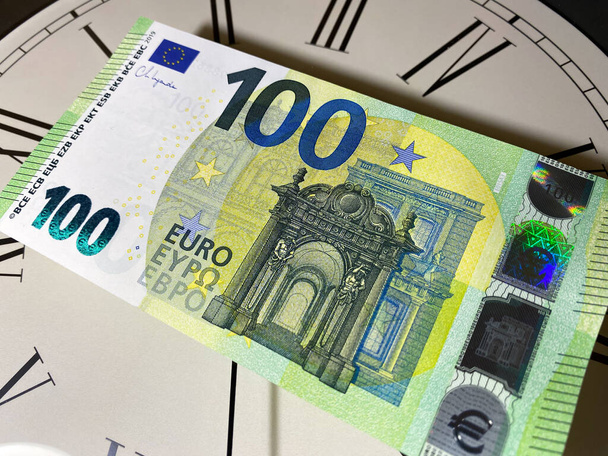 Новая сотня евро 2013 года стоит на часах, на циферблате с римскими цифрами. Время деньги. - Фото, изображение