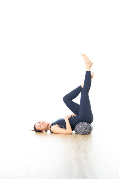 Відновлювальна йога з блискавкою. Молода спортивна приваблива жінка в яскраво-білій студії йоги, лежить на блискучій подушці, розтягується і розслабляється під час реставраційної йоги. Здоровий активний спосіб життя
 - Фото, зображення