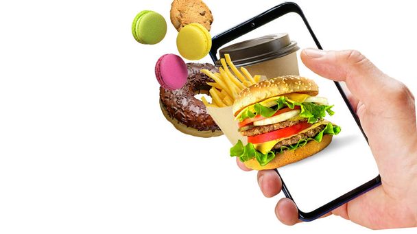Kézben tartó telefon hamburger sült krumpli kávéscsésze fánk repül ki a képernyőn elszigetelt fehér alapon. Online rendelés gyorsétterem. - Fotó, kép