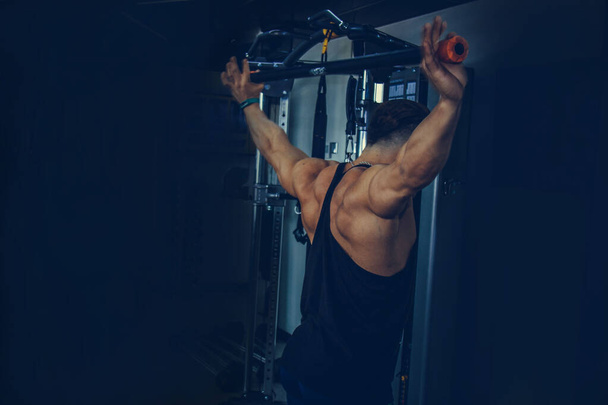 a man with big muscles is engaged in weightlifting in the gym. A pumped-up athlete goes in for sports on heavy weight simulators. sport exercises. - 写真・画像