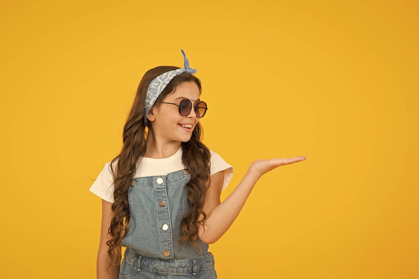 retro girl presenting product. small kid wear summer outfit. cheerful child has vintage look. headkerchief and sunglasses - summer accessory. beauty and fashion. happy childhood. copy space - Zdjęcie, obraz