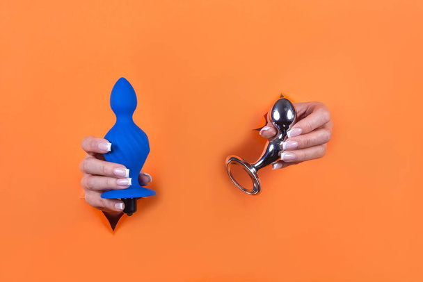 Adult sex toys in women's hands on an orange background. - Фото, зображення