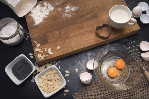 Bakery process. Healthy baking ingredients - flour, almond nuts, eggs, milk on the black background. Top view. Modern cooking composition. Kitchen utensils. - Foto, Imagen