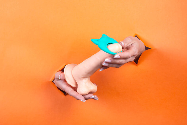 Adult sex toys in women's hands on an orange background. - Foto, afbeelding