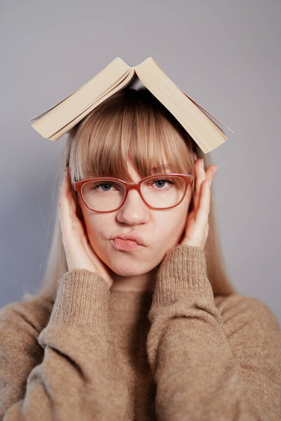 Сомневаюсь студентка с книгой на голове и очках - Фото, изображение