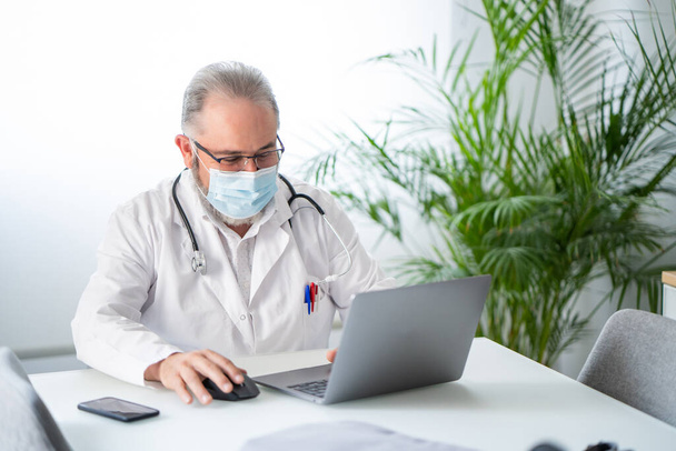 Doctor working with laptop in his office. Telematic or online work concept. - Foto, imagen