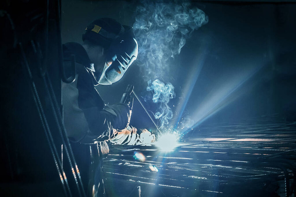 Un ouvrier masqué effectue des travaux de soudage sur des structures métalliques dans une usine ou une entreprise industrielle. - Photo, image