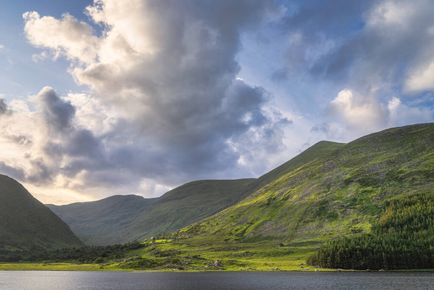 Jezioro Gummeenduff i skaliste wzgórza MacGillycuddys Reeks góry oświetlone przez ciepłe światło zachodu słońca w Black Valley, Ring of Kerry, Irlandia - Zdjęcie, obraz