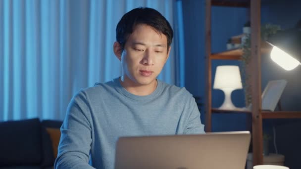 Asia freelance zakenman focus werken typen op laptop computer online op afstand van bedrijf op bureau in de woonkamer thuis overuren 's nachts, Werk vanuit huis tijdens COVID-19 pandemie concept. - Video