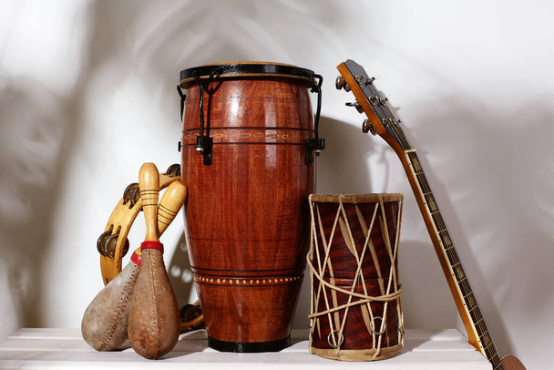 Composition of musical ethnic instrument. Maracas, tambourine, conga, guitar and ethnic drum. Percussion rhytm instruments under palm shade. Cuban sound, latin culture, samba and rumba - Foto, imagen