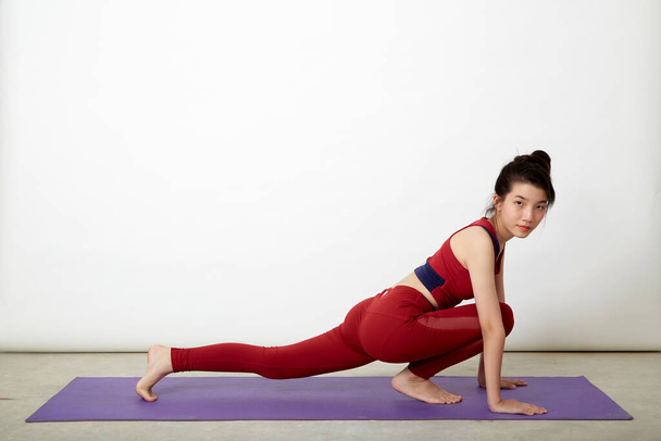 Mujer asiática haciendo pose sobre esterilla de yoga, ejercitándose en estudio - Foto, imagen