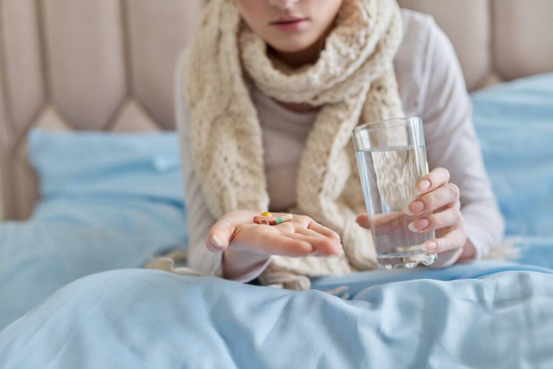 Female taking pills, capsules with glass of water, at home in bed - Fotó, kép